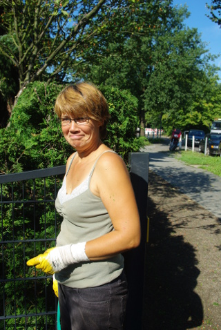 Gärtnerin mit Handschuhen vor einem Gartentor
